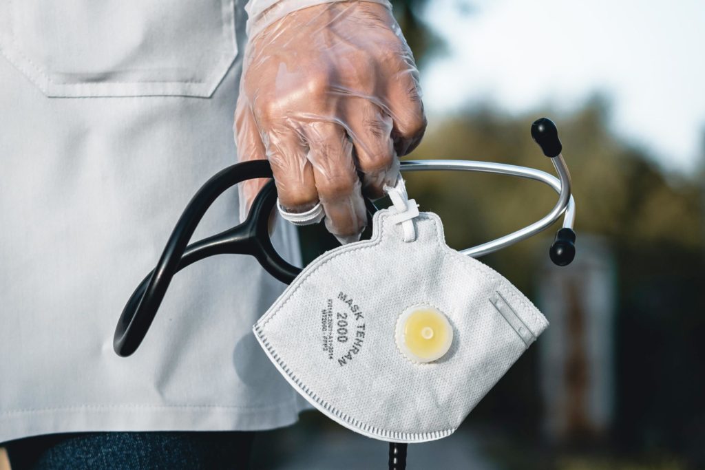 a gloved hand holding a mask and stethoscope