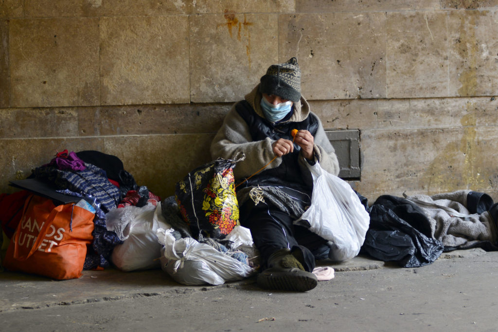 Homeless woman in medical mask sits in an underground passage near a closed subway.